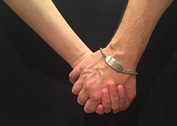 a pair of clasped hands, one of which has a silver medical ID bracelet on it