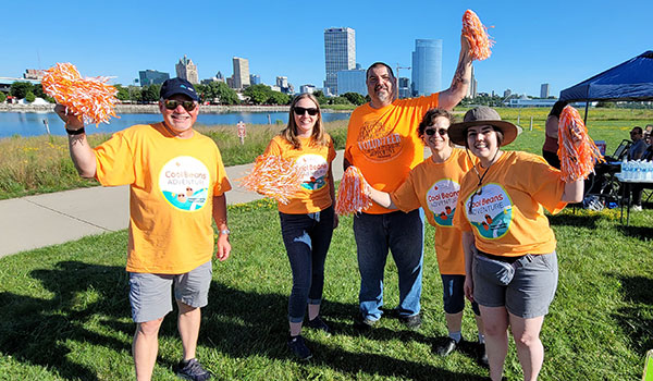 5 NKFW volunteers wearing orange Cool Beans t-shirts and waving orange and white pompoms
