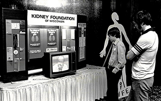 historical black and white photo of a man and older boy viewing a health fair display table